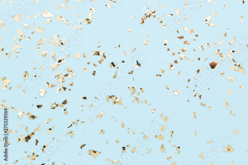 Golden foil confetti on light blue background. Festive, party or holiday glowing backdrop. Flat lay, top view.