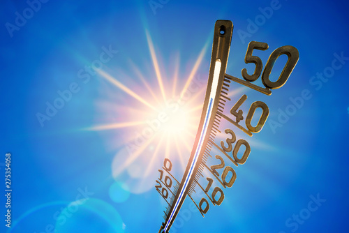 Hot summer or heat wave background, bright sun on blue sky with thermometer