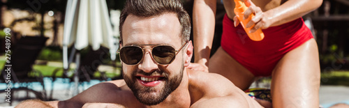 panoramic shot of woman holding bottle with sunblock near happy man in sunglasses