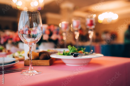 Table served for special occasion. Empty plate, glasses, forks, napkin and flowers on table covered with white tableclothes. Elegant dinner table. White table setting