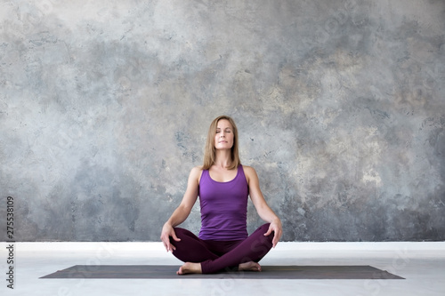 Caucasian woman practicing yoga, doing sukhasana or easy seat pose, working out. Indoor full length studio shot