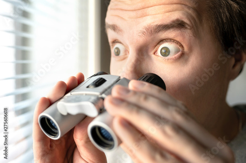 Surprised man with binoculars. Curious guy with big eyes. Nosy neighbour stalking or snooping secrets, gossip and rumour. Silly funny face. Shocked about unbelievable news. Stalker peeping people.