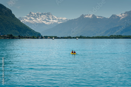 Swiss Alps mountain and Lake Geneva landscape with tourist paddling on the lake in a yellow kayak