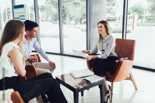 Financial advisor showing report to young couple for their investment. Salesman and positive couple talking about purchase. Happy couple consulting financial agent for loan.