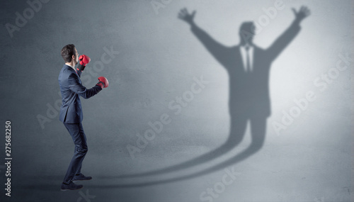 Businessman with boxing gloves fighting with disarmed businessman shadow 