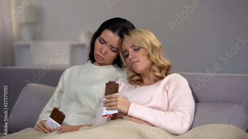 Two upset female friends eating chocolate, support after relations brake-up