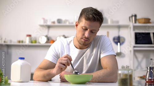 Unhappy lonely man looking with disgust at food in bowl, lack of appetite