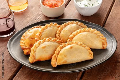 A closeup of Argentinian empanadas with sauces and wine on a dark rustic wooden background