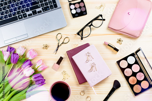 Feminine office desk with stationery, laptop, fashion accessories, flowers and make up products. Woman work desk lay out