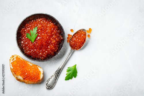 Delicious red caviar in black bowl on a light concrete background. Top view with copy space. Flat lay