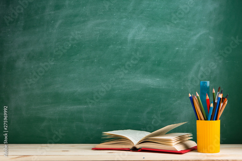 Education and reading concept - group of colorful books on the wooden table in the classroom, blackboard background