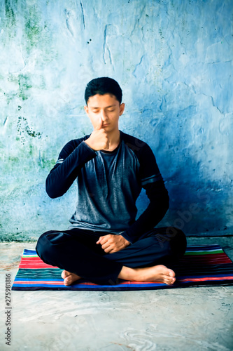 Portrait shot of the young man doing pranayama or pranayam or breath control yoga on a colorful mat with wearing black attire.