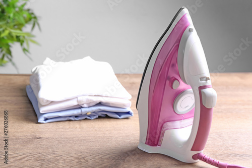 Modern electric iron and folded clothes on wooden table against light background. Space for text