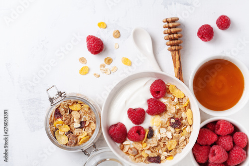 Greek yogurt in bowl with raspberries, honey and muesli on white stone table top view. Healthy diet breakfast.