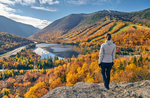 Woman hiking at Artist's Bluff in autumn. View of Echo Lake. Fall colours in Franconia Notch State Park. White Mountain National Forest, New Hampshire, USA