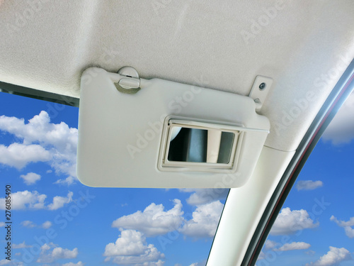 Car sun visor and mirror in car with sky and clouds as a backdrop.