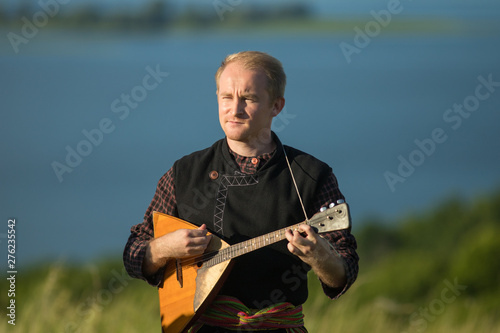 A man in traditional russian clothes playing balalaika on the field