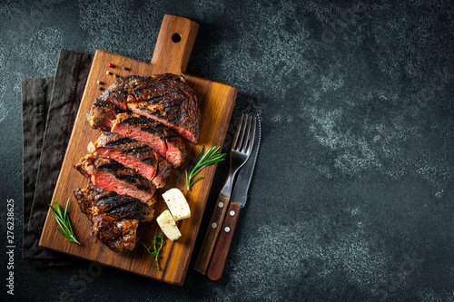 Sliced steak ribeye, grilled with pepper, garlic, salt and thyme served on a wooden cutting Board on a dark stone background. Top view with copy space. Flat lay
