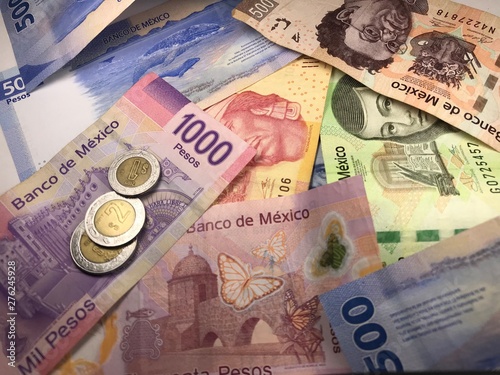 Many mixed Mexican peso bills spread over a wooden desk