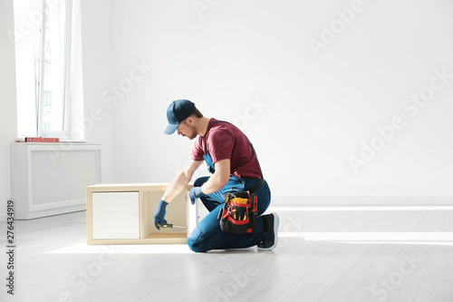 Handyman in uniform assembling furniture indoors, space for text. Professional construction tools