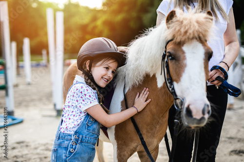 Cute little girl and her older sister enjoying with pony horse outdoors at ranch.
