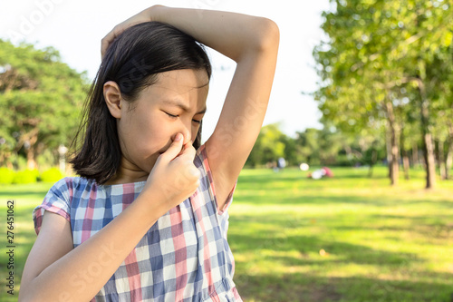 Asian cute girl feel bad foul odor situation,smelling,sniffing her wet armpit in outdoor park,beautiful child feeling smell of sweat, problems due to hormonal changes,motion facial expression reaction