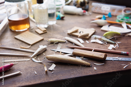 Wood working. Wood carving. Making handcrafted fishing lures form balsa wood.Hand made fishing lures on a work table with tools in background. Shallow depth of field. Focus on foreground.