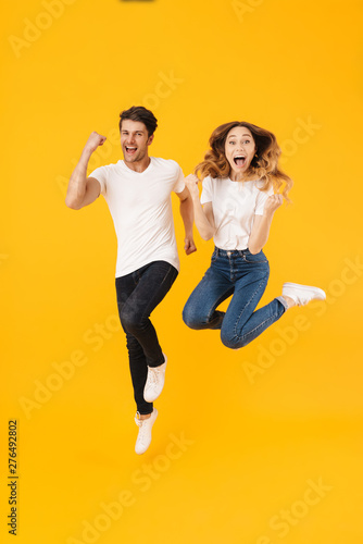 Full length portrait of beautiful couple man and woman in basic t-shirts rejoicing while clenching fists