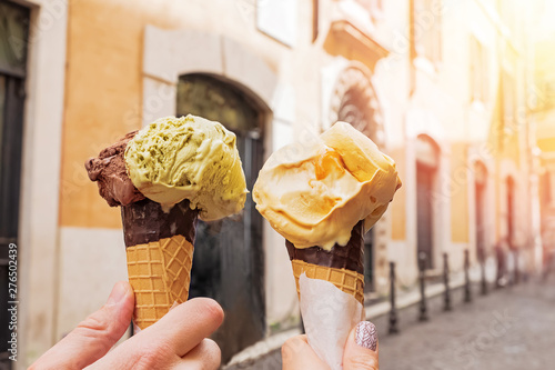Two hands close-up holding cones with italian ice-cream gelato on the background of Rome streeet