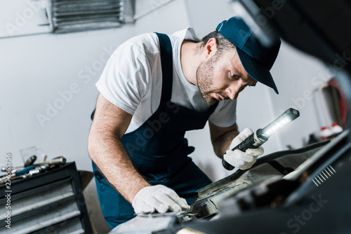 selective focus of bearded car mechanic holding flashlight near car