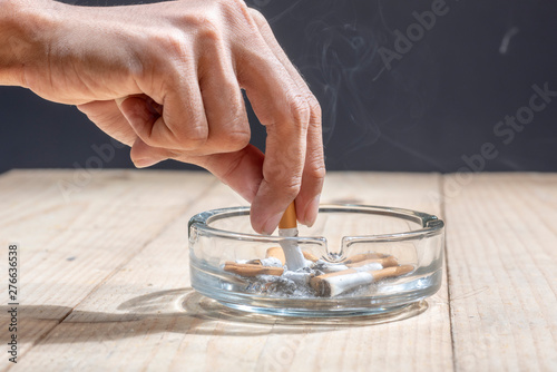 Hand stubbed out cigarette in a transparent ashtray