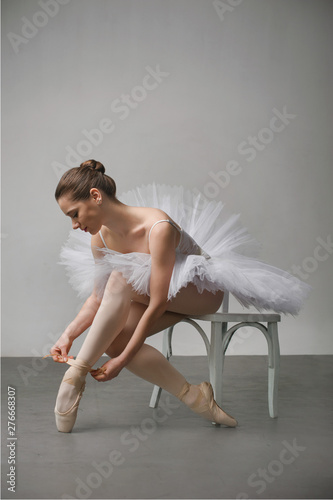 ballerina in a white dress sitting on a chair and tying her ballet slippers, for wall background.
