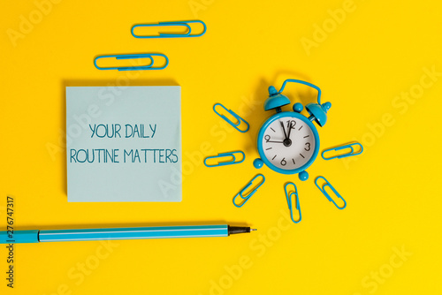 Word writing text Your Daily Routine Matters. Business photo showcasing practice of regularly doing things in fixed order Metal alarm clock wakeup clips ballpoint notepad colored background