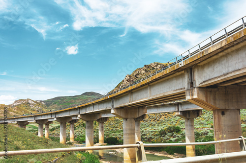 Two road turn highway bridge, viaduct supports in the valley among the green hills, transport infrastructure.