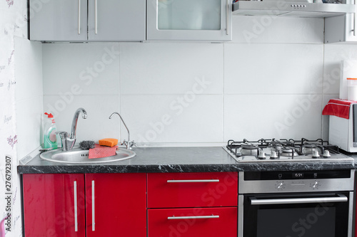 Beautiful modern clean red kitchen in small apartment full shot. Empty cuisine after washing interior of cooking area with stove and sink for washed dishes