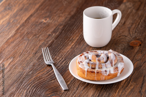 Large gourmet frosted cinnamon roll on brown distressed table.