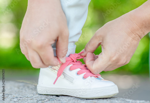 Happy family. Close up mother helping her little daughter to tie shoelaces on summer day