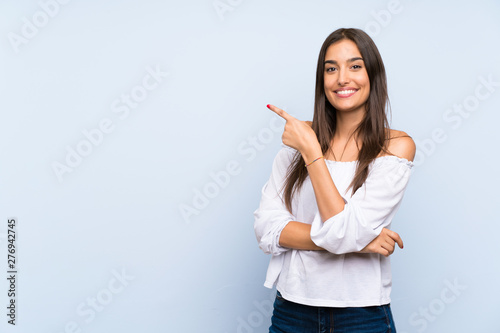 Young woman over isolated blue background pointing finger to the side