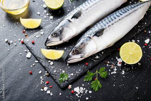 Fresh fish. Mackerel with salt, lemon and spices on black stone background. 