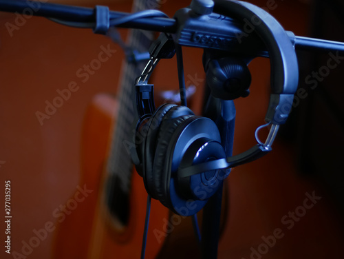 Black studio headphones on a stand and black guitar background.
