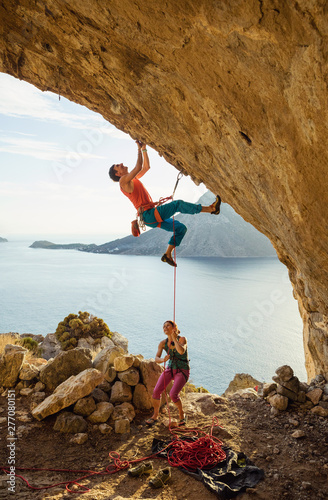 Young man starts climbing challenging route, his female partner belaying him
