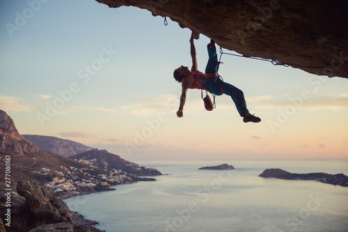 Young man struggling to climb challenging route on cliff