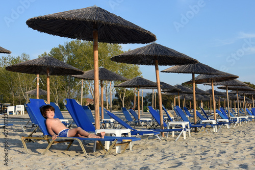 Little boy enjoy in deck chairs on the beach during vacations. Child on summer beach with parasols