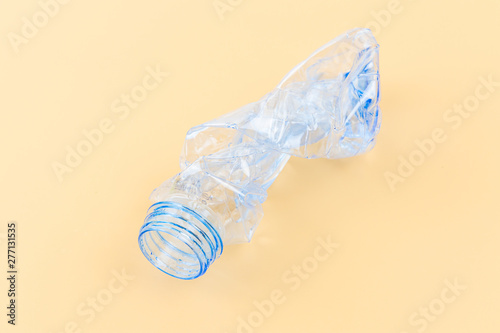 A single crushed empty and clean PET plastic bottle. Close up shot on light colour background without cap and label.