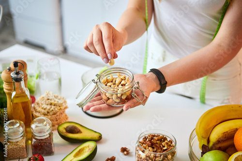 Young happy woman eating different nuts (cashew, hazelnut, almond) in modern kitchen. Healthy food and Dieting concept. Loosing Weight