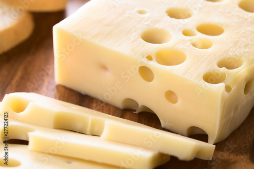 Piece of Emmental, Emmentaler or Emmenthal cheese on wooden plate (Selective Focus, Focus one third into the cheese piece)