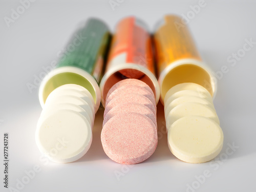 Three kinds of soluble effervescent vitamins spilled out of plastic bottles on a white background. Under a sunlight. Vitamins and nutritional supplements. Health care and medical.