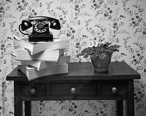 Old black rotary dial telephone on stack of phone books, black and white