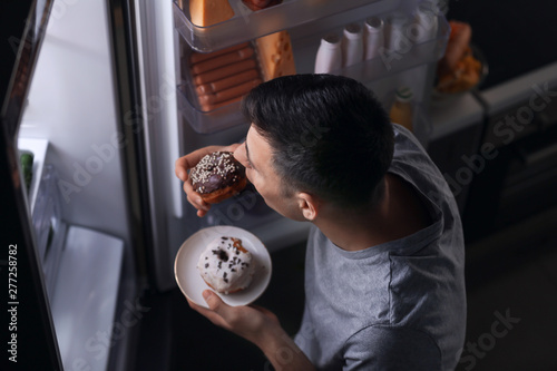 Young man eating food near refrigerator at night