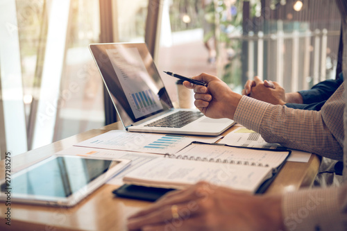 Business partnership pointing to the graph of the company financial statements report and profits earned during in the computer screen with giving a presentation to colleagues in office room.